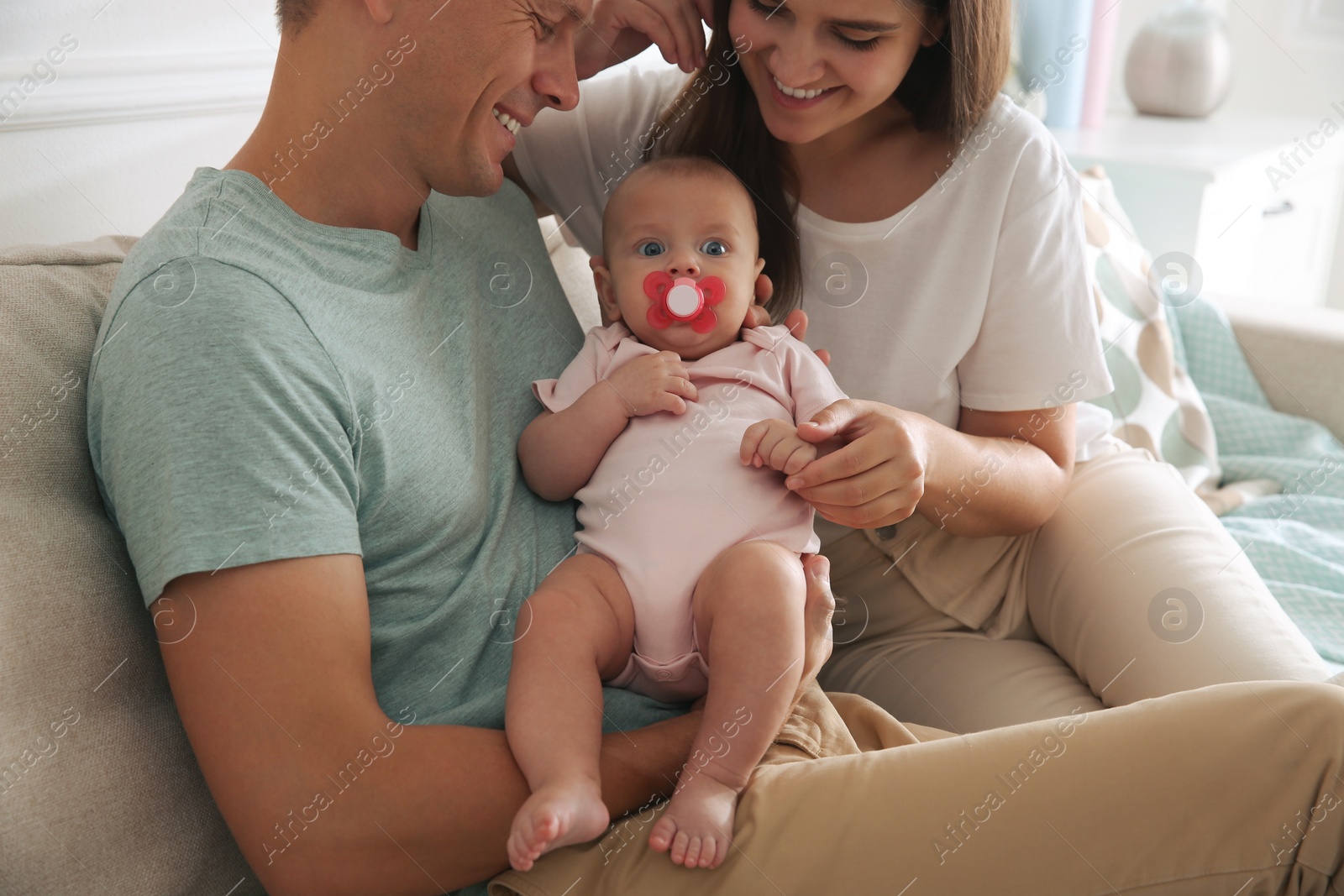 Photo of Happy couple holding their cute little baby with pacifier at home