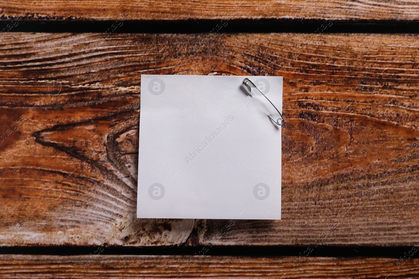 Photo of Paper sheet attached with safety pin on wooden table, top view. Space for text