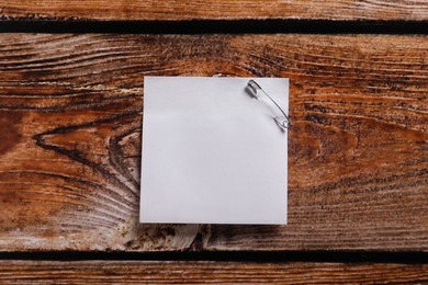 Photo of Paper sheet attached with safety pin on wooden table, top view. Space for text