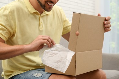 Happy man opening parcel on sofa at home, closeup. Internet shopping