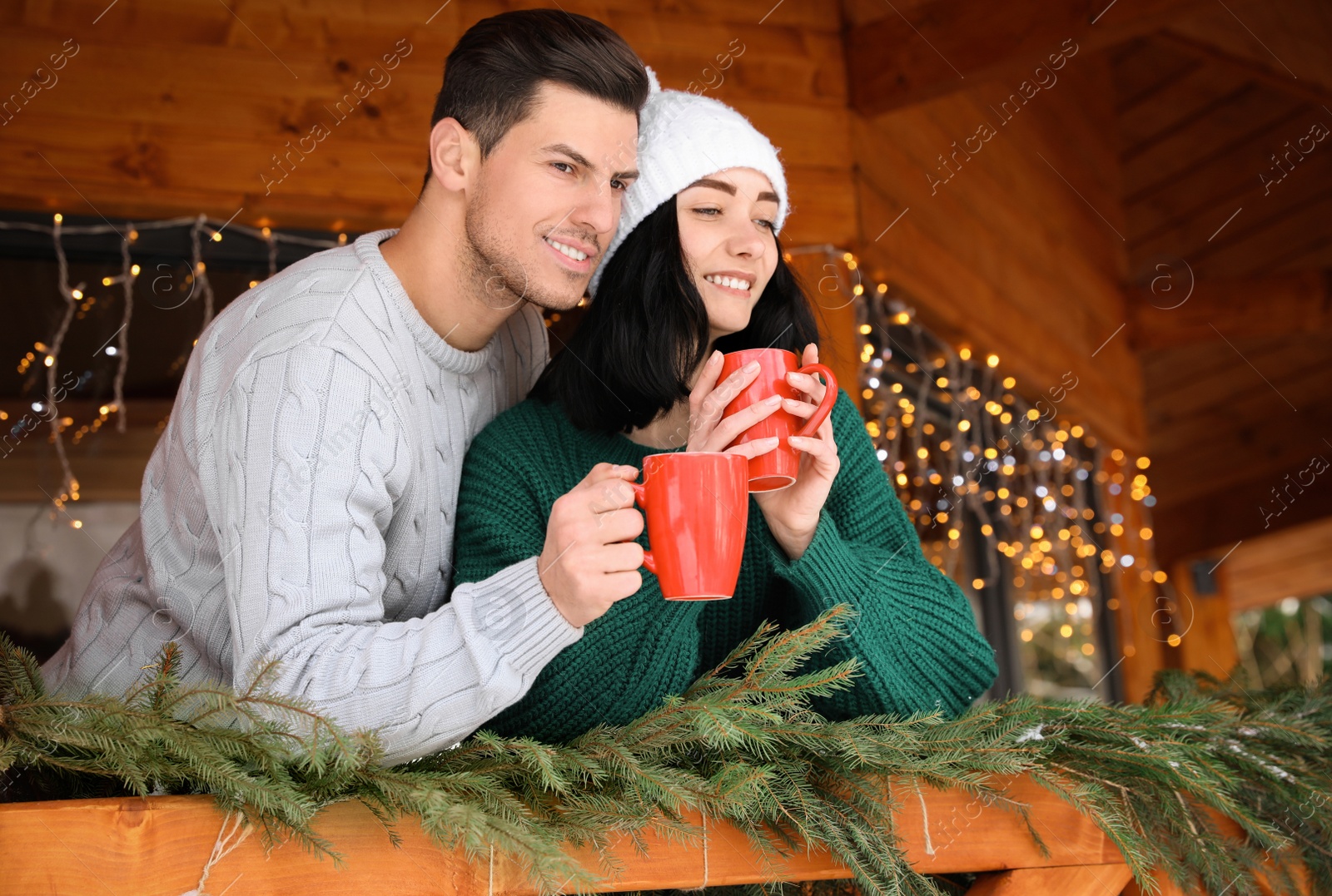 Photo of Happy couple in sweaters with cups near decorated railing