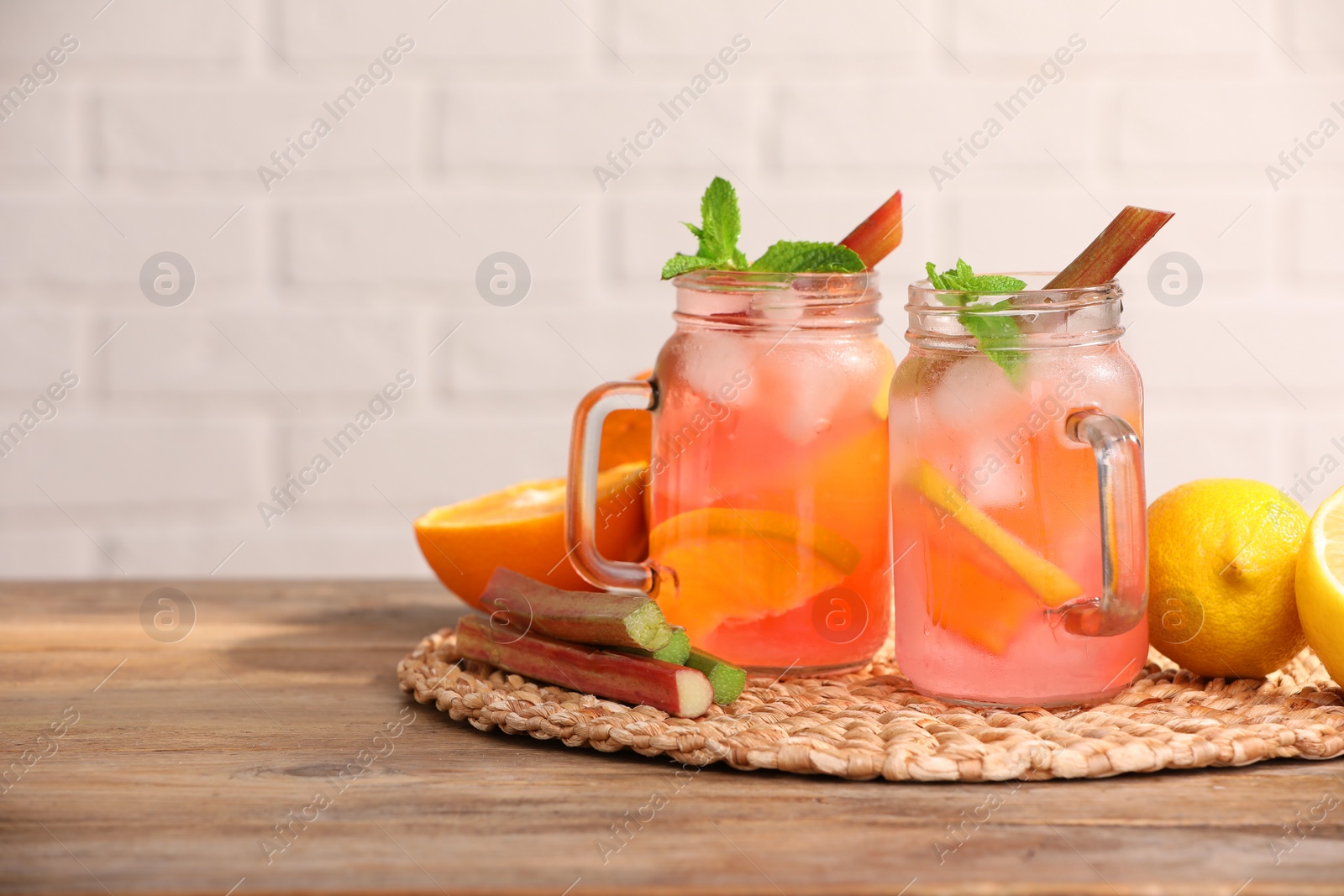 Photo of Mason jars of tasty rhubarb cocktail with citrus fruits on wooden table, space for text