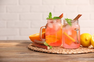 Photo of Mason jars of tasty rhubarb cocktail with citrus fruits on wooden table, space for text