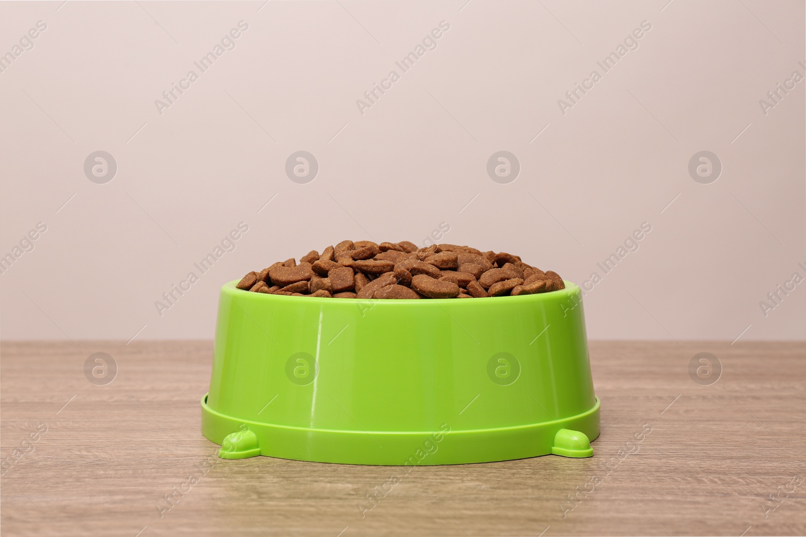Photo of Dry food in green pet bowl on wooden surface