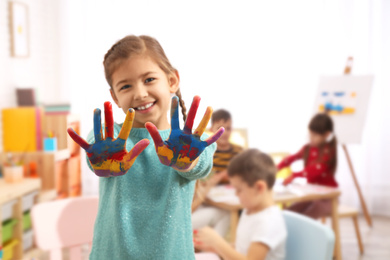 Photo of Cute little child with painted palms in room, focus on hands