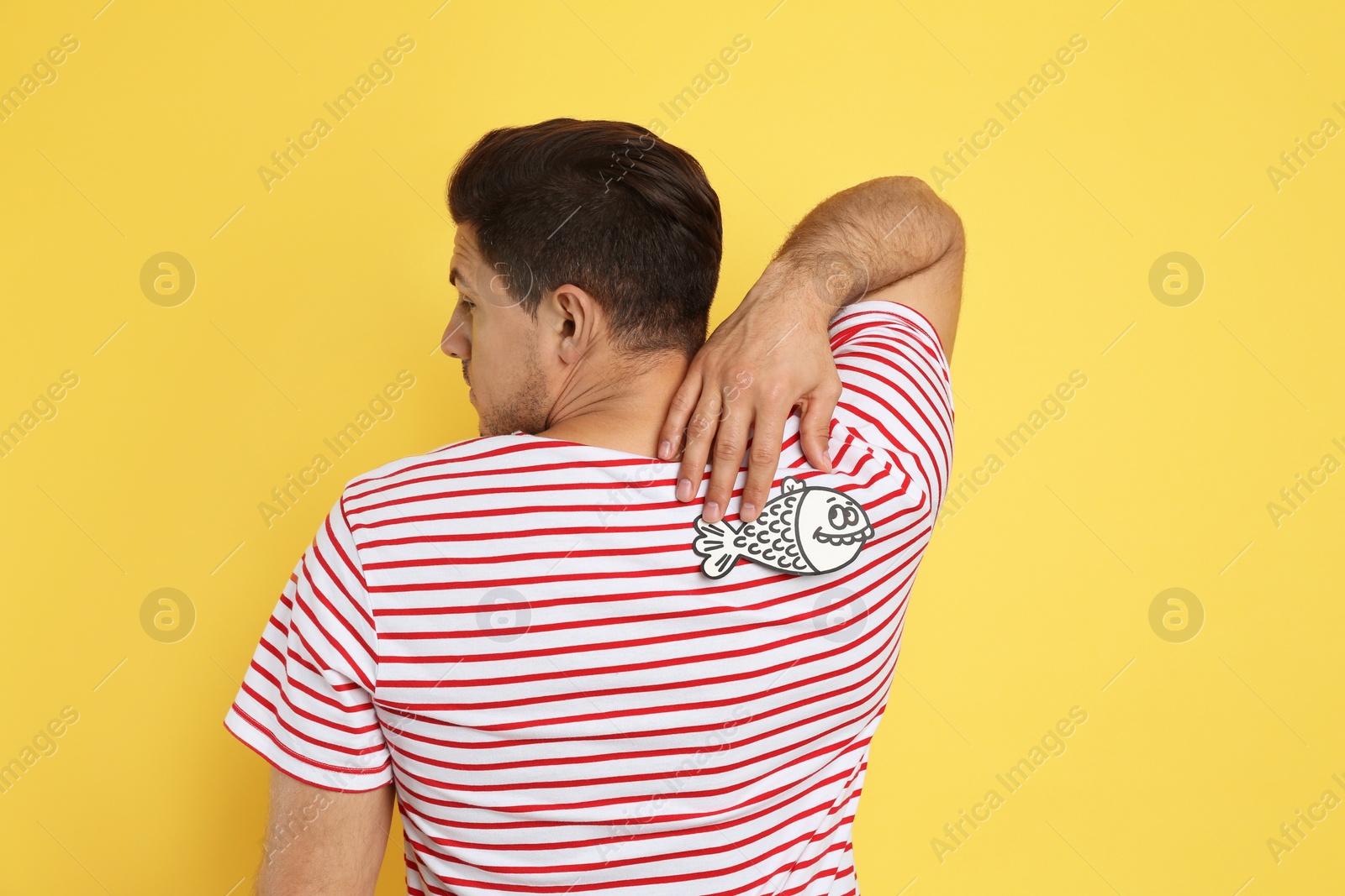 Photo of Man with paper fish on back against yellow background. April fool's day