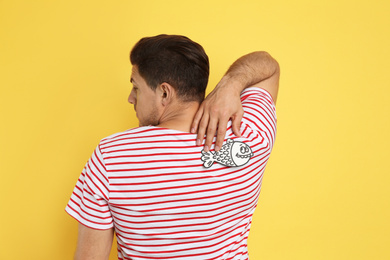 Photo of Man with paper fish on back against yellow background. April fool's day