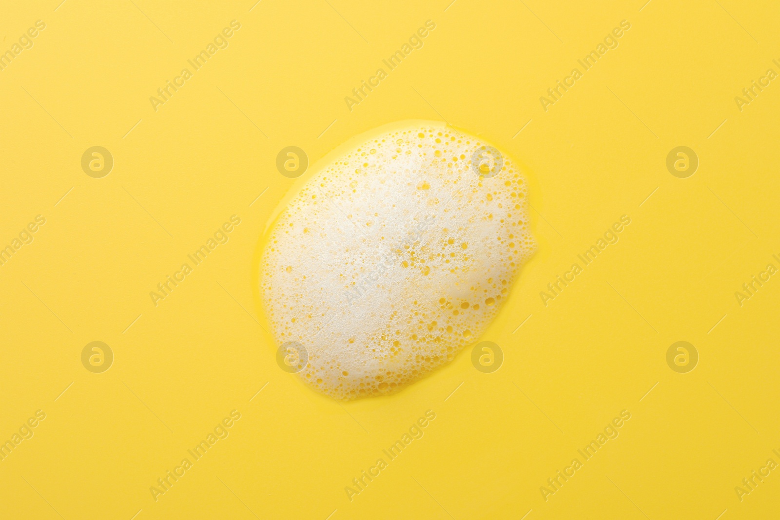 Photo of Drop of fluffy soap foam on yellow background, top view