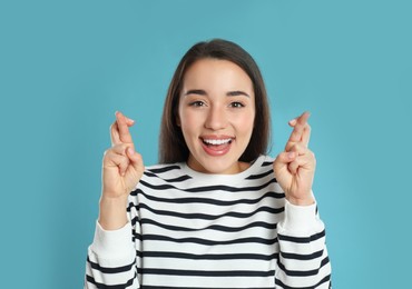 Photo of Woman with crossed fingers on light blue background. Superstition concept