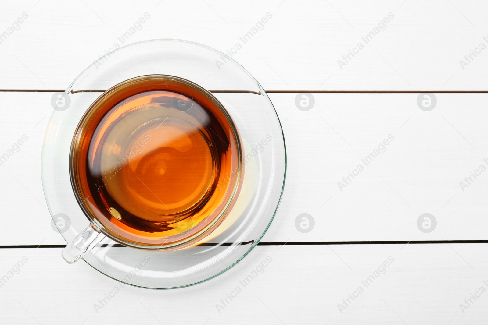 Photo of Glass cup of tea on white wooden table, top view. Space for text