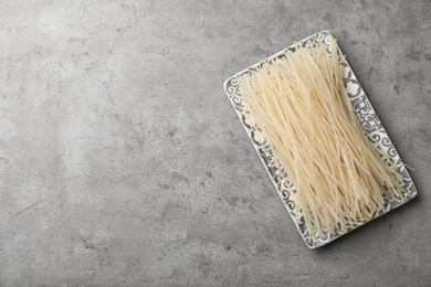 Photo of Plate with raw rice noodles on grey background, top view. Space for text