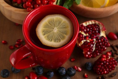 Photo of Cup with delicious immunity boosting tea and ingredients on wooden table, closeup