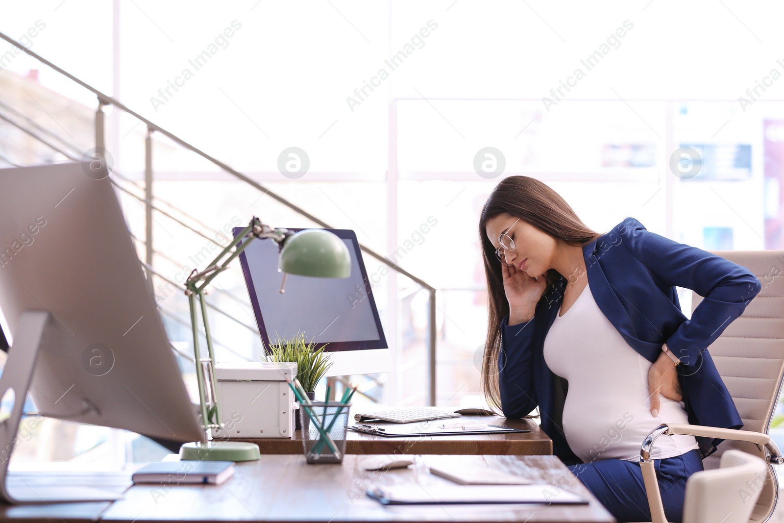 Photo of Young pregnant woman suffering from pain while working in office