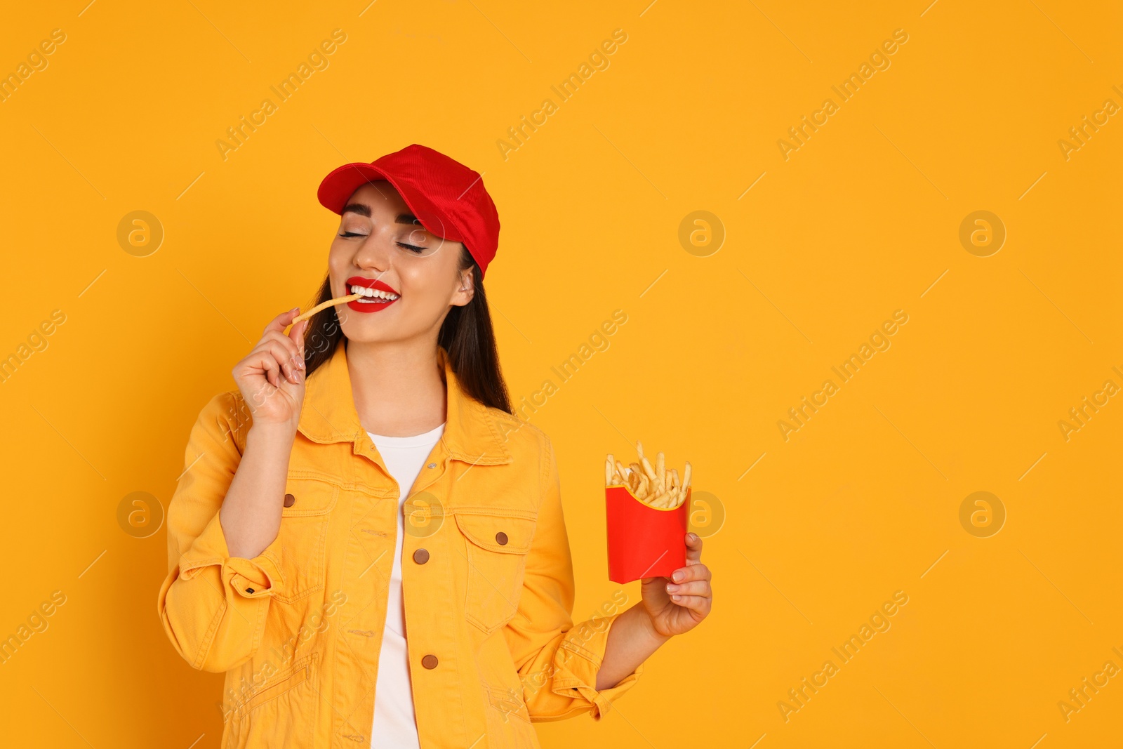 Photo of Beautiful young woman eating French fries on yellow background. Space for text