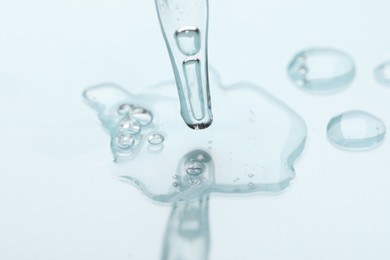 Photo of Glass pipette and transparent liquid on light background, closeup