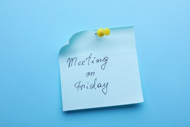 Photo of Paper note with words Meeting on Friday pinned to light blue background