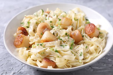 Photo of Delicious scallop pasta with spices in bowl on gray textured table, closeup