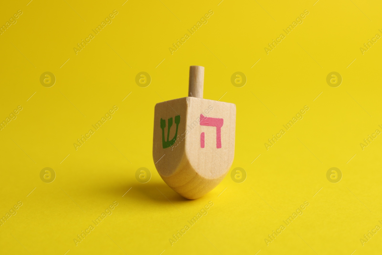 Photo of Wooden dreidel on yellow background. Traditional Hanukkah game