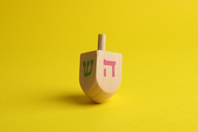 Photo of Wooden dreidel on yellow background. Traditional Hanukkah game