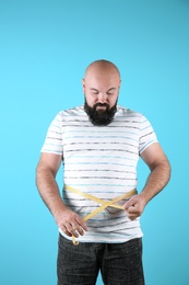 Fat man with measuring tape on color background. Weight loss