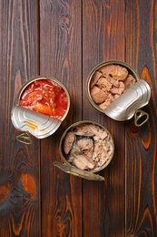 Photo of Tin cans with fish on wooden table, flat lay