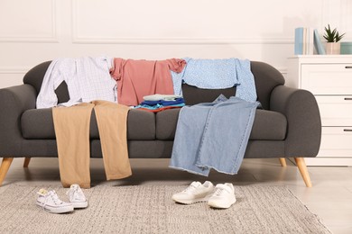 Shoes near sofa with different clothes indoors