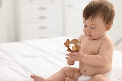 Cute baby boy with wooden rattle on bed at home. Space for text