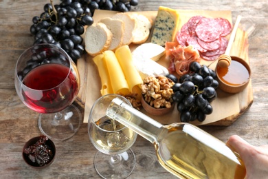 Photo of Woman pouring white wine into glass on table with delicious food, closeup