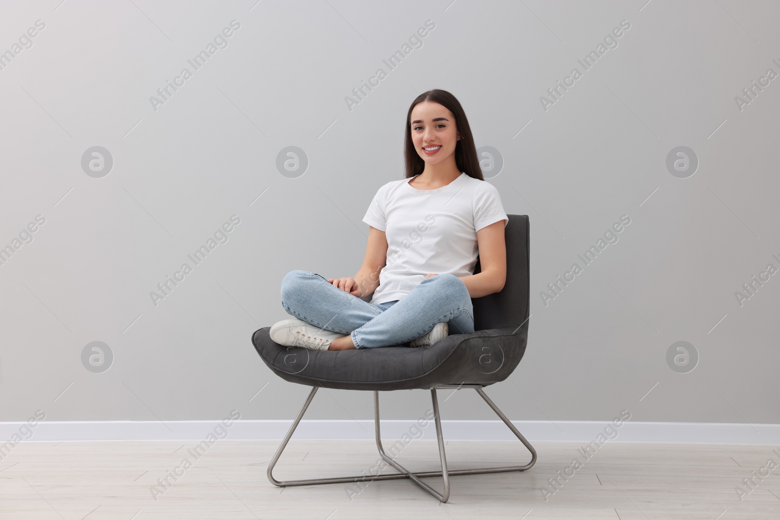 Photo of Beautiful woman sitting in armchair near light grey wall indoors