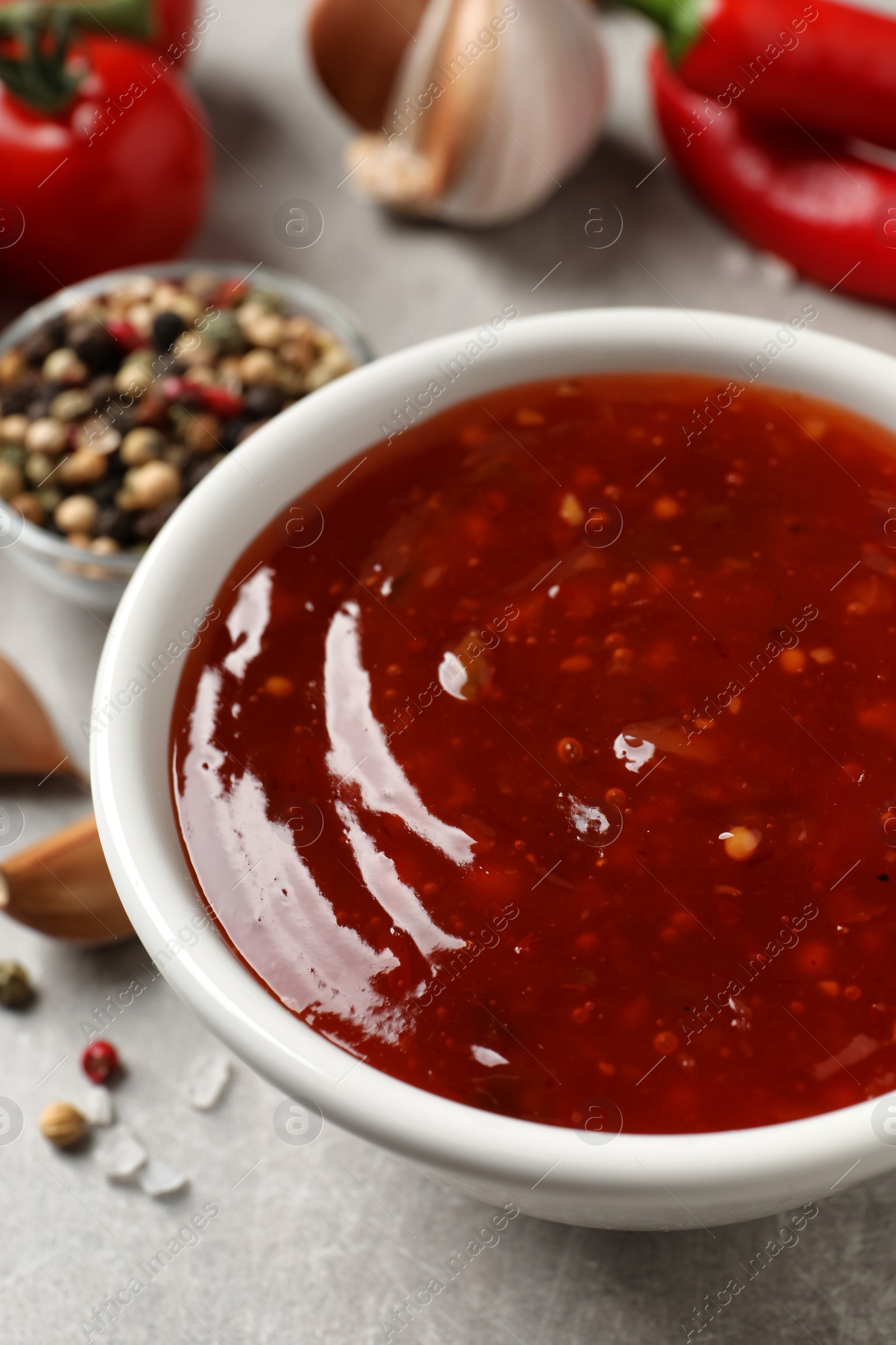 Photo of Spicy chili sauce in bowl on grey table, closeup