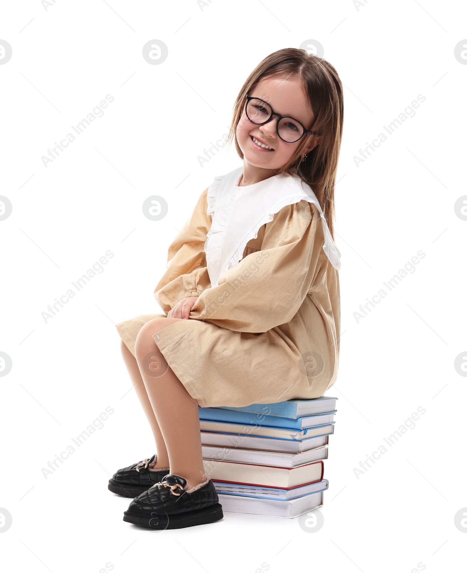 Photo of Cute little girl in glasses sitting on stack of books against white background