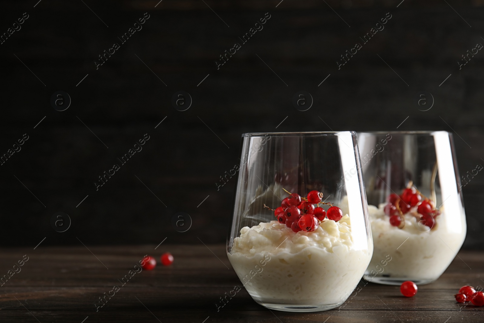 Photo of Creamy rice pudding with red currant in glasses and berries on wooden table. Space for text