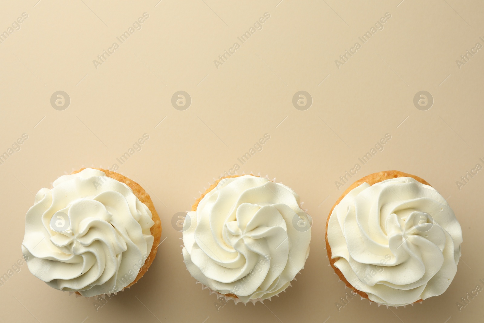 Photo of Tasty vanilla cupcakes with cream on beige background, top view. Space for text