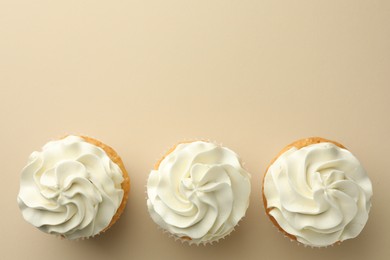 Tasty vanilla cupcakes with cream on beige background, top view. Space for text