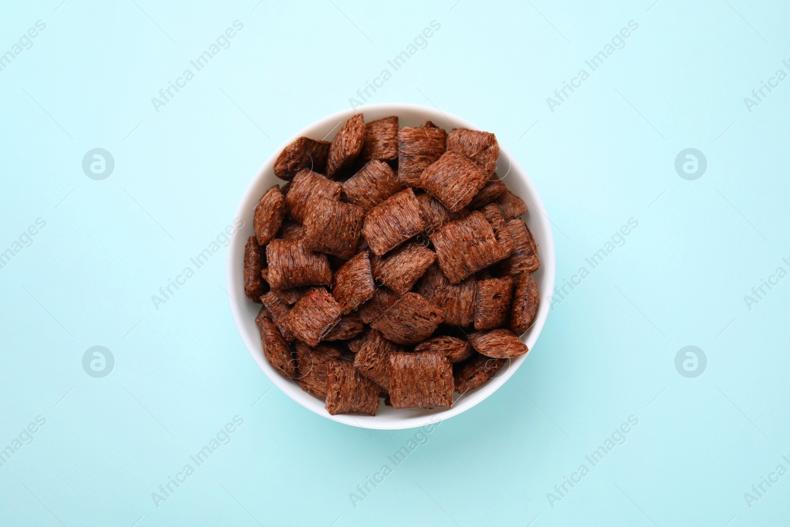 Photo of Chocolate cereal pads in bowl on light blue table, top view