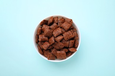 Photo of Chocolate cereal pads in bowl on light blue table, top view