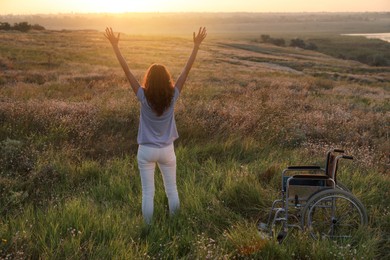 Photo of Woman standing near wheelchair in evening outdoors, back view. Healing miracle