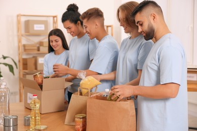 Photo of Group of volunteers packing food products at table in warehouse