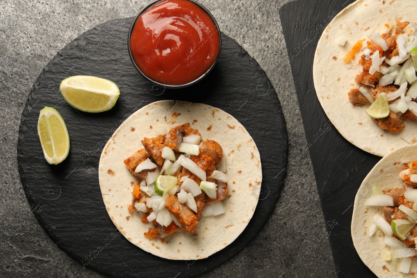 Photo of Delicious tacos with vegetables, meat and ketchup on grey textured table, flat lay