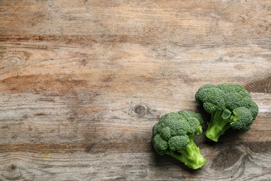 Photo of Fresh raw broccoli florets on wooden table, top view with space for text