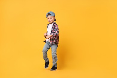 Photo of Happy little boy dancing on yellow background. Space for text