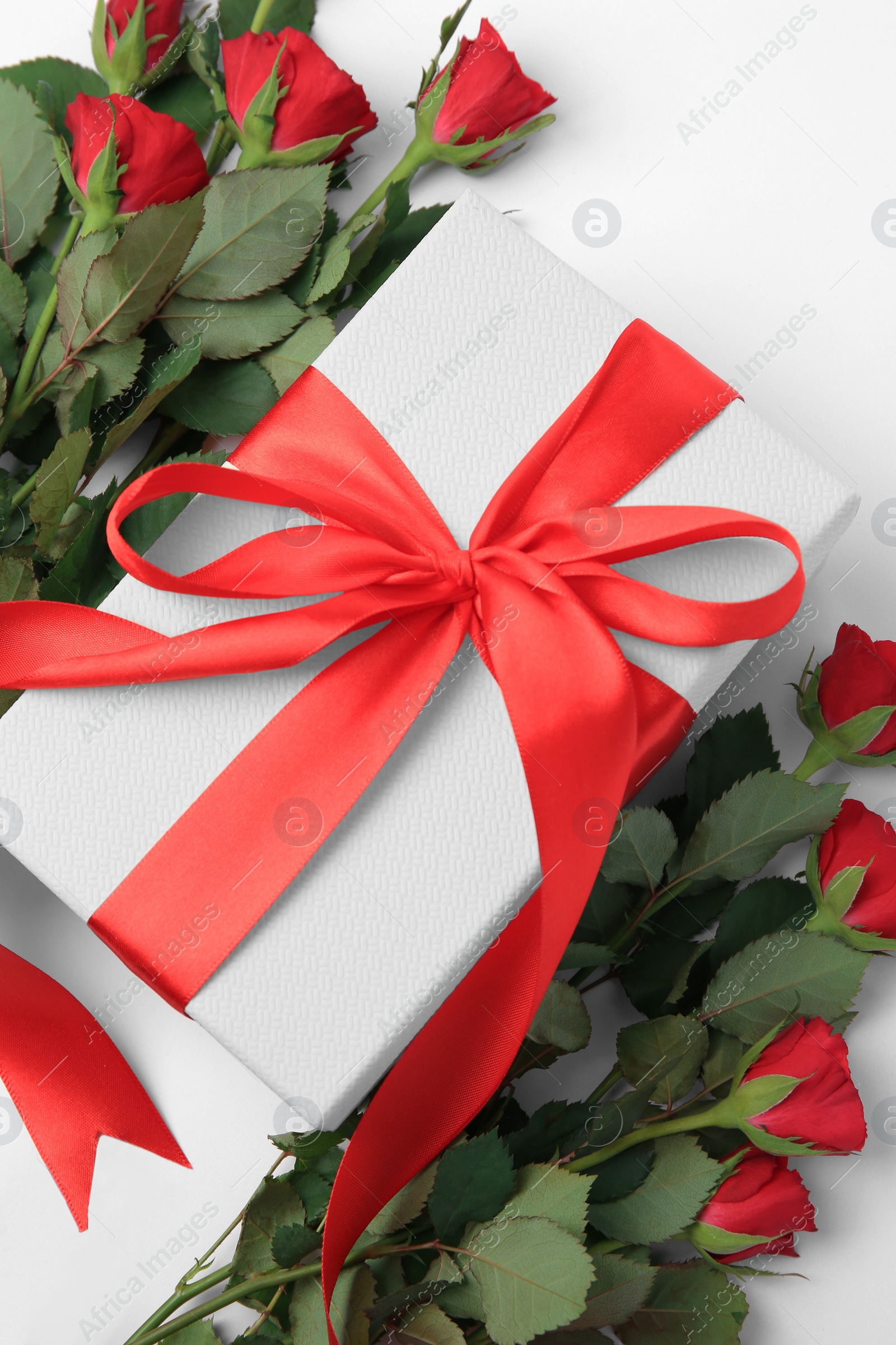 Photo of Beautiful gift box with bow and red roses on white background, flat lay