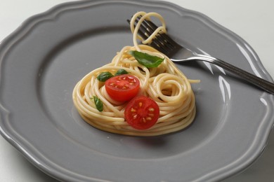 Photo of Heart made of tasty spaghetti, fork, tomato and basil on white table, closeup