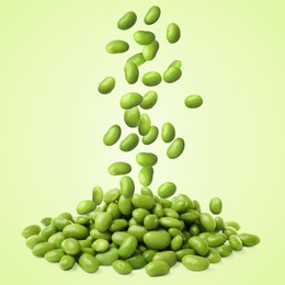 Delicious edamame soybeans falling onto pile against light green background