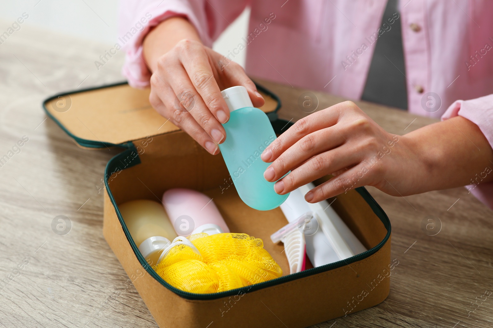 Photo of Woman packing cosmetic travel kit into compact toiletry bag at wooden table, closeup. Bath accessories