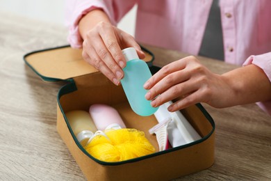 Woman packing cosmetic travel kit into compact toiletry bag at wooden table, closeup. Bath accessories