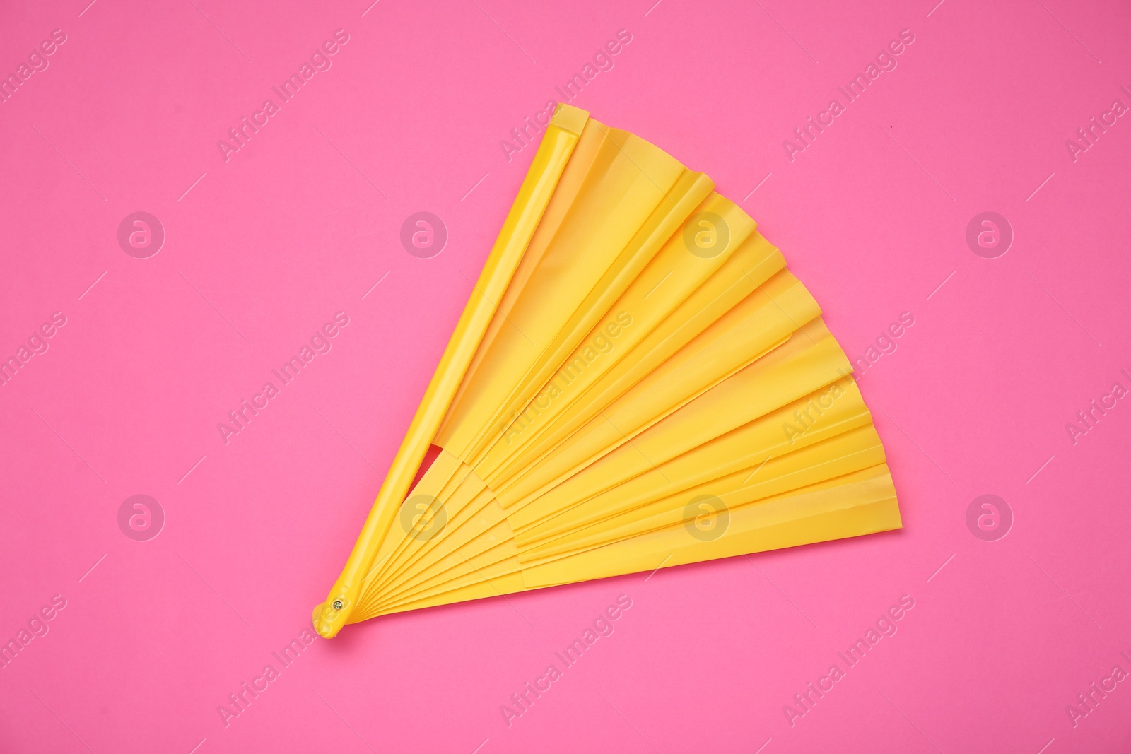 Photo of Bright yellow hand fan on pink background, top view