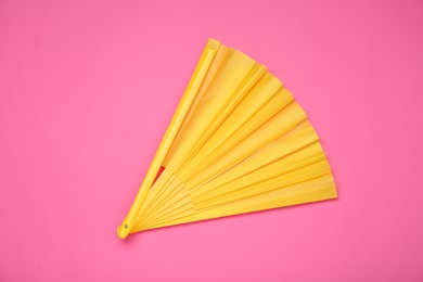 Photo of Bright yellow hand fan on pink background, top view