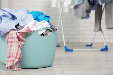 Plastic laundry basket overfilled with clothes in bathroom. Space for text