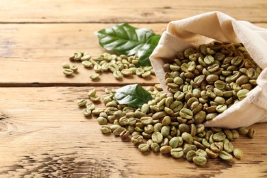 Photo of Sackcloth bag with green coffee beans and leaves on wooden table, space for text